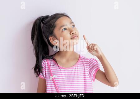 Ritratto di una bambina asiatica che indossa un abito a righe rosa e bianco. Il bambino che mostra il dito indice sinistro sembra ottenere l'idea per qualcosa A. Foto Stock