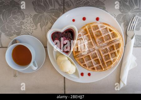 Vista superiore del tavolo della colazione con waffle belgi, gelato e marmellata di frutti di bosco con tè in una tazza. Ristorante con pasti dolci leggeri, che serve, stile Foto Stock