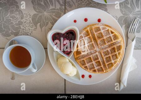 Vista superiore del tavolo della colazione con waffle belgi, gelato e marmellata di fragole con tè in una tazza bianca. Ristorante leggero con cibi dolci Foto Stock