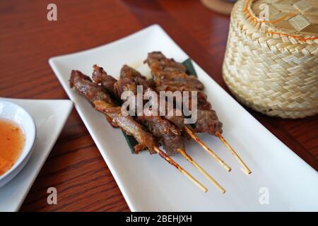 Spiedini di maiale al barbecue serviti con un cesto di legno di riso appiccicoso, ricetta tailandese Foto Stock