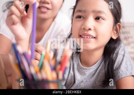 Figlia e madre stanno raccogliendo matite colorate nella scatola. Ragazza asiatica piccola e una donna che seleziona un colore per la pittura. Foto Stock