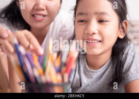 Figlia e madre stanno raccogliendo matite colorate nella scatola. Ragazza asiatica piccola e una donna che seleziona un colore per la pittura. Foto Stock