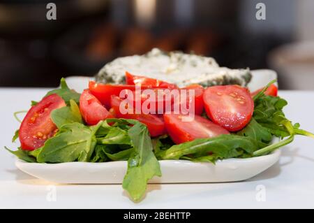 Primo piano di pomodori ciliegini dimezzati con foglie di razzo servite su piatto bianco Foto Stock