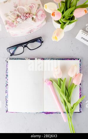 Luogo di lavoro dallo stile femminile con tulipani, occhiali e notebook. Foto Stock