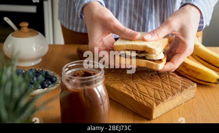 Sandwich con burro e banana spalmati al cioccolato. Mani femminili con gustosa colazione dolce o pranzo sandwich con cioccolato alla nocciola spalmato e gres Foto Stock