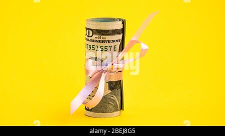 Piccolo regalo del dollaro, pacchetto delle fatture di cento dollari legati con un nastro rosa. Dollari isolati su sfondo giallo Foto Stock