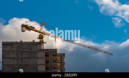 Gru industriale vicino edificio contro cielo blu con belle nuvole. Cantiere. Contesto industriale. Foto Stock