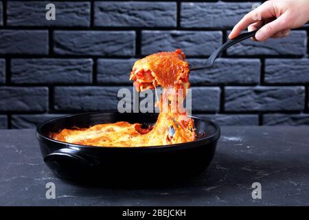 Donna tiene a mano spatola da cucina con una porzione di cannelloni italiani con salsa di bolognese e mozzarella sopra su un piatto nero o Foto Stock