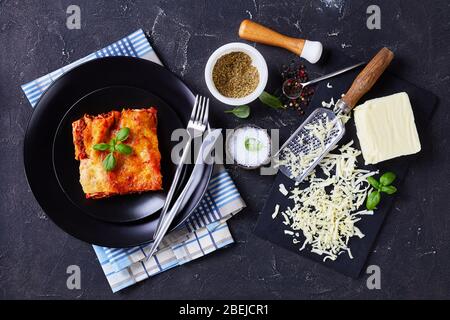 Una porzione di cannelloni di pasta ripieni con salsa di manzo e mozzarella su un piatto nero su fondo di cemento scuro con b fresco Foto Stock