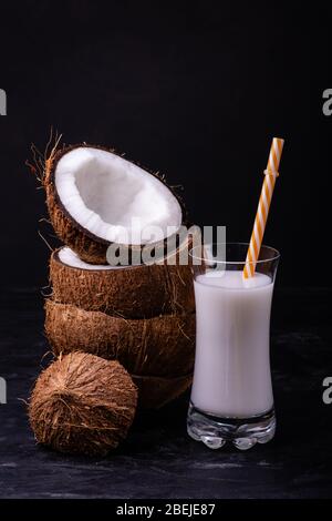 vista frontale, alcuni pezzi di cocco impilati e latte di cocco nel bicchiere, su sfondo scuro Foto Stock