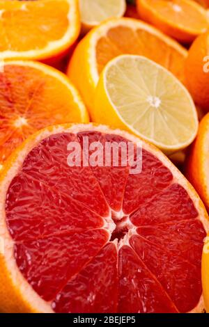 in primo piano mezzo pompelmo rosso fresco e succoso, sullo sfondo altri agrumi misti a fette Foto Stock