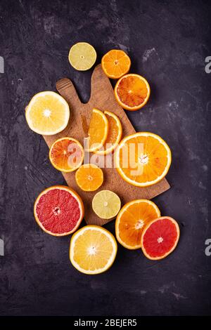 vista dall'alto di vari tipi di agrumi, tagliati a fette e disposti su uno sfondo rustico, nero Foto Stock