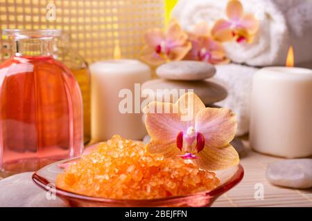 Centro benessere. In primo piano, un sale da bagno orchido e aranciato. In fondo candele, pietre impilate, asciugamani bianchi e bottiglie con Foto Stock