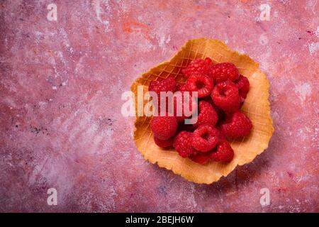 vista dall'alto di alcuni lamponi freschi nel wafer del gelato sullo sfondo rustico e variegato Foto Stock