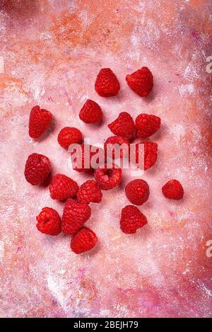 vista dall'alto, su uno sfondo ruvido colorato con macchie rosse, alcuni lamponi freschi. Foto Stock