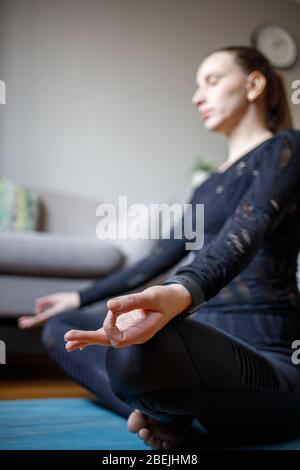 Giovane donna che pratica la meditazione yoga a casa quarantena. Messa a fuoco ravvicinata Foto Stock