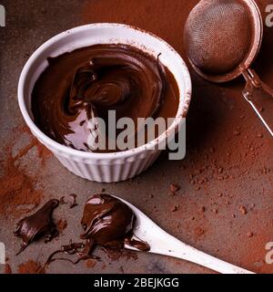 ciotola in ceramica con crema di cioccolato fondente, cucchiaio spalmato di cioccolato e cosparso di cacao sullo sfondo Foto Stock