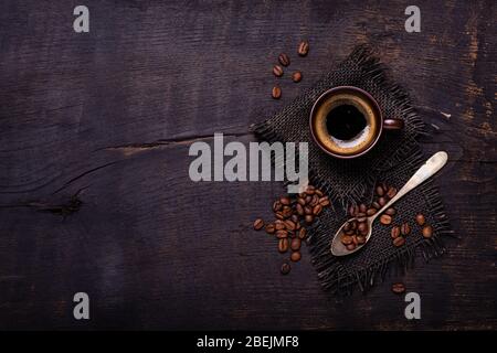 visto dall'alto. Sul tavolo di legno ruvido e scuro, una tazza di caffè con un cucchiaio di chicchi di caffè. Spazio per copiare Foto Stock
