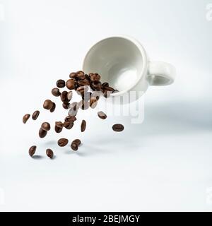 isolata da fondo bianco, una tazza di caffè sospesa nell'aria da cui scorre una cascata di chicchi di caffè tostati Foto Stock