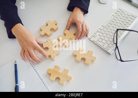 Mani senza volto di una donna d'affari con puzzle di legno su un tavolo bianco in Office.with finestre. Analisi della strategia del team di pianificazione soluzione di idea conce Foto Stock