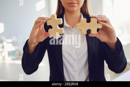 Mani senza volto di una donna d'affari con puzzle in legno in mani in ufficio. Foto Stock