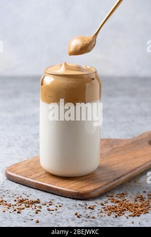 Caffè Dalgona in vetro con cucchiaio su grigio. Caffè espresso in latte con schiuma di caffè istantaneo. Inquadratura verticale. Foto Stock