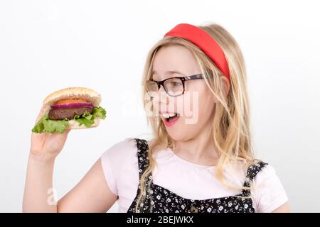 Giovane ragazza bionda che indossa occhiali in una banda rossa Alice tenendo un hamburger fatto in casa Foto Stock