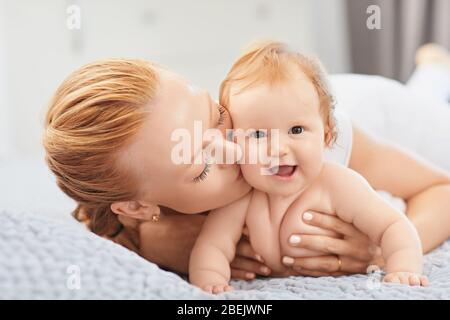 La madre felice sorride al bambino sdraiato a letto in camera. Foto Stock