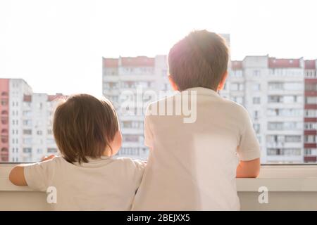 I bambini sono costretti a stare a casa durante la quarantena relativa alla pandemia di covid-19, fratelli si guardano sulla città finestra aperta del balcone Foto Stock