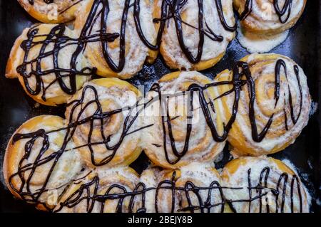 Cinnabon. Rotoli di cannella decorati con cioccolato su un vassoio di cottura. I panini dolci sono piatti. Foto Stock