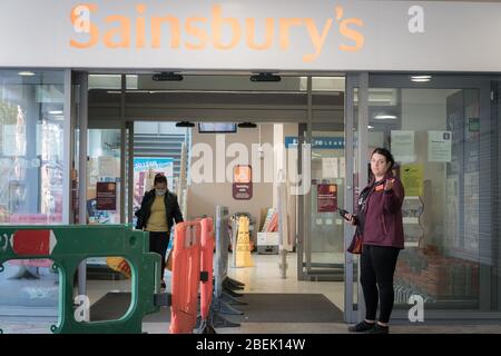 Redhill, Surrey, Regno Unito - 10 aprile 2020 - Marchal all'ingresso di un supermercato regola il numero di acquirenti nel negozio per garantire le distanze sociali Foto Stock