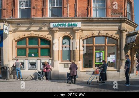 Redhill, Surrey, Regno Unito - 10 aprile 2020 - persone che accodano ad una macchina di cassa, mantenendo le distanze sociali per fermare la diffusione del coronovirus Foto Stock