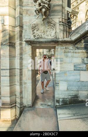 Milano, Italia - 1 agosto 2019. Un giovane in occhiali da sole con una borsa sulla cintura si erge sul tetto del Duomo di Milano in Italia. Orientamento selettivo verticale. Foto Stock