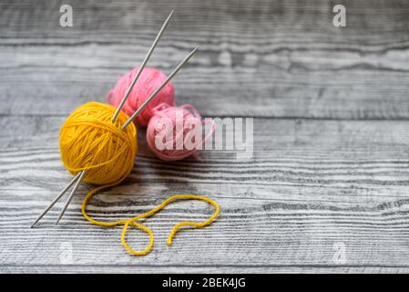 Piatto di tre palle di lana colorate, aghi di maglia che posano sullo sfondo di legno. Foto Stock