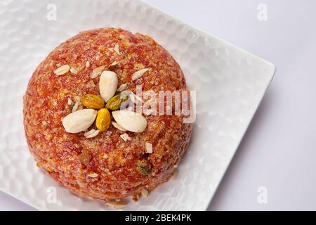 Gajar ka halwa tenuto su un piatto bianco con frutta secca decorata sulla parte superiore. Foto Stock