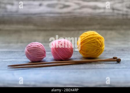 Piatto di tre palle di lana colorate, aghi di maglia che posano sullo sfondo di legno. Foto Stock