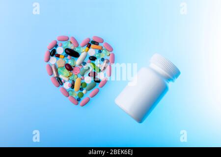 Pillole multicolore a forma di cuore e vaso di plastica su sfondo blu gradiente. Forma del cuore fatta di compresse, concetto di trattamento e. Foto Stock