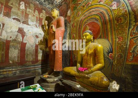 Scultura di uno dei primi re dello Sri Lanka accanto alla statua di un Buddha seduto nell'antica grotta tempio buddista di Rangiri Dambulu Raja ma Foto Stock