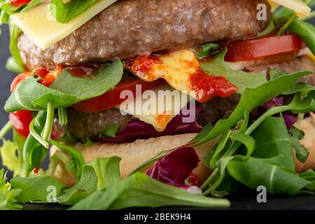 Doppio cheeseburger con molta rucola e salse - vista ravvicinata Foto Stock