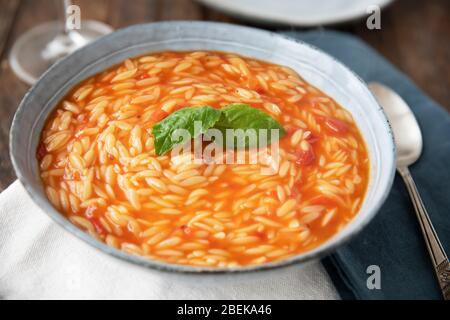 Ciotola di pasta all'orzo e zuppa di pomodoro con basilico Foto Stock