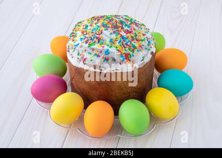 Torta di Pasqua e uova multicolore dipinte su tavole di legno bianche. Cartolina di saluto Paschal. Sfondo chiaro, texture platks Foto Stock