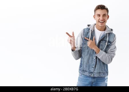 Ritratto di bel biondo uomo in giacca denim, puntando le dita a sinistra come presentazione pubblicità, raccomandare link o prodotto, sorridente fotocamera, consigli Foto Stock