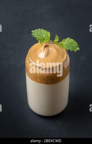 Dalgona caffè in vetro con crema melissa su nero. Trend korean bere latte freddo con schiuma di caffè istantaneo. Inquadratura verticale. Foto Stock