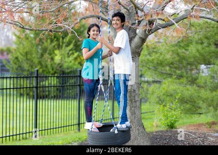 Ritratti di fratelli su un pneumatico che ruota all'aperto in primavera Foto Stock