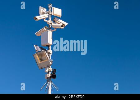 Palo con diverse telecamere di sicurezza e sensori di movimento contro un cielo blu chiaro Foto Stock