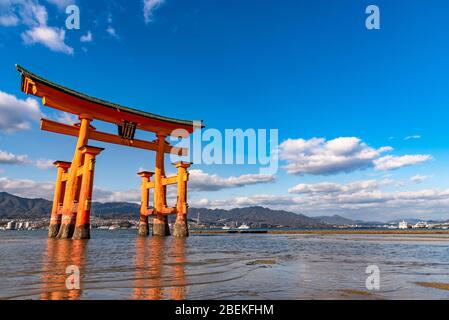 Il gigante rosso arancione galleggiante Grand o-Torii porta si trova nella baia di Miyajima spiaggia a bassa marea di fronte al santuario di Itsukushima in giornata di sole. Hiroshima Foto Stock