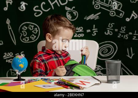 Primo giorno di scuola. Ragazzo di scuola elementare. Ritorno a scuola. Il ragazzino raccoglie lo zaino della scuola a scuola. Bambino di scuola elementare. Foto Stock