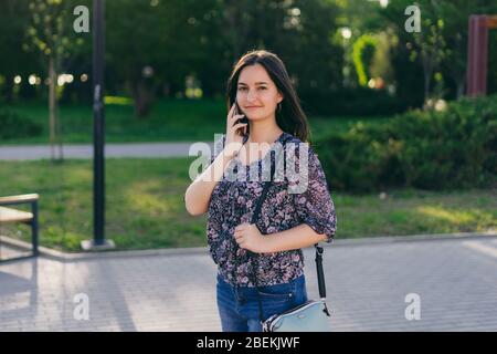 Ragazza con telefono cammina per la città. Donna brunetta con borsetta in vicolo. Foto Stock