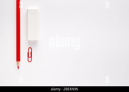 Forniture di cancelleria su sfondo bianco. Matita rossa, gomma e graffetta. Concetto di semplicità. Foto Stock