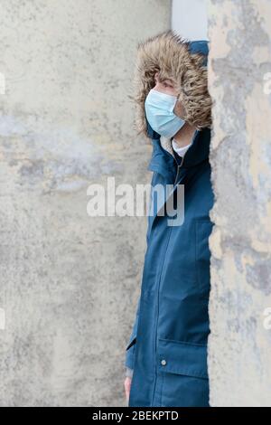 Uomo malsano con cappuccio protettivo monouso contro le malattie infettive trasmissibili e come protezione contro l'influenza o il coronavirus Foto Stock